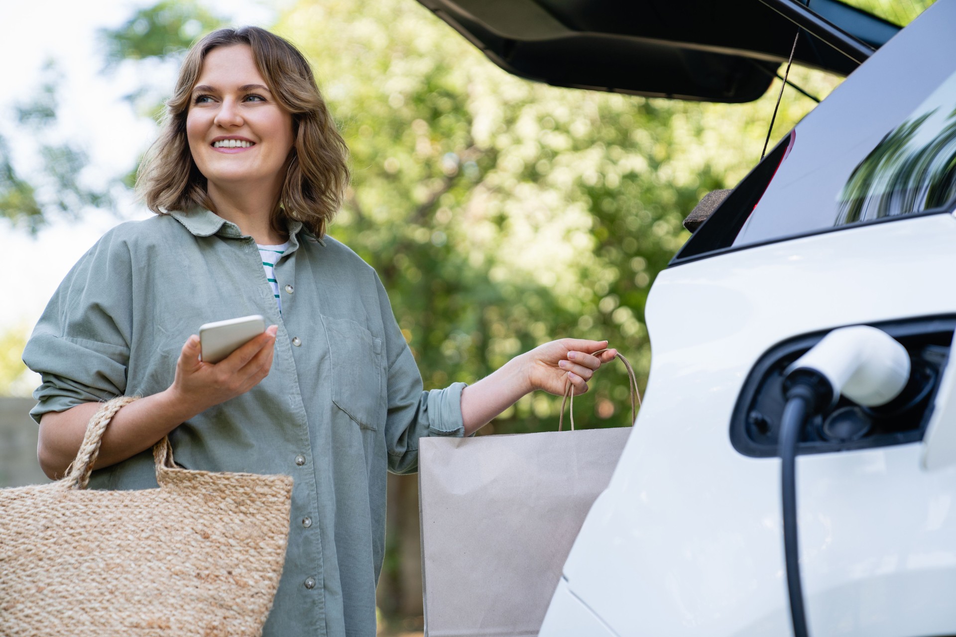 Woman with shopping bag next to a charging electric car